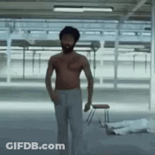 A Shirtless Man With A Beard Is Standing In A Room Holding A Stool . GIF