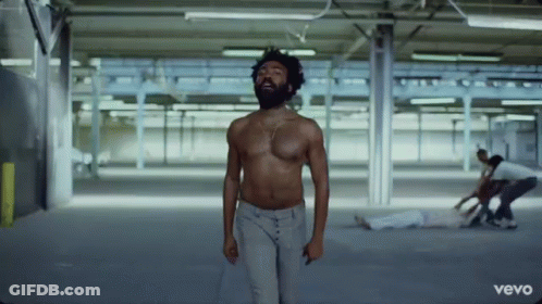 A Shirtless Man With A Beard Is Standing In A Warehouse . GIF