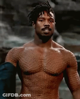 A Shirtless Man With A Beard Is Standing In Front Of A Rock Wall . GIF