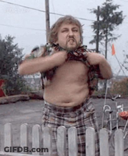 A Shirtless Man With A Beard Is Standing Next To A Fence And Taking Off His Shirt . GIF