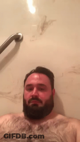 A Shirtless Man With A Beard Is Taking A Bath In A Tub . GIF