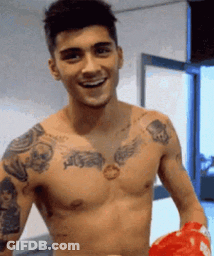 A Shirtless Man With A Lot Of Tattoos On His Chest Is Holding A Red Boxing Glove . GIF