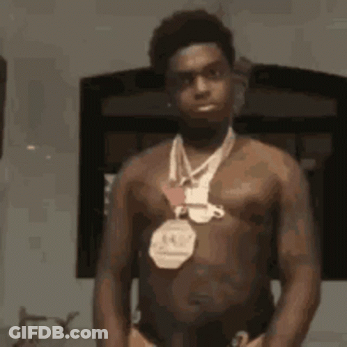 A Shirtless Man With A Medal Around His Neck Is Standing In Front Of A Mirror . GIF