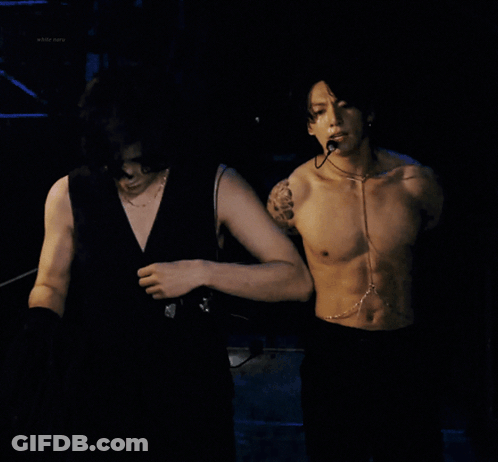 A Shirtless Man With A Microphone Around His Neck Looks At The Camera GIF