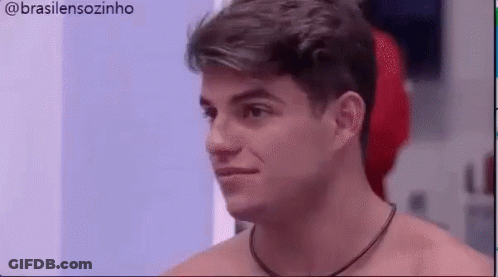 A Shirtless Man With A Necklace Around His Neck Is Looking At Something . GIF