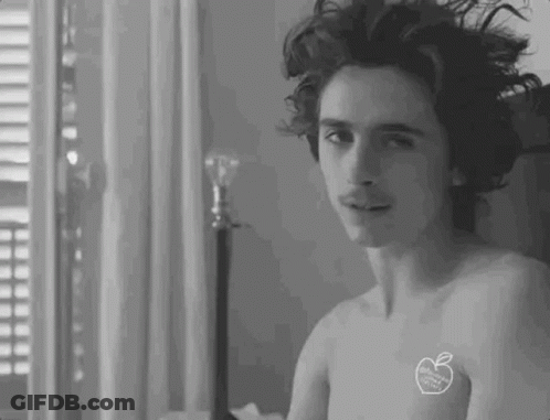 A Shirtless Man With A Sticker On His Chest Is Sitting On A Bed . GIF