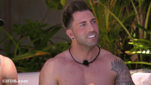 A Shirtless Man With A Tattoo On His Arm Is Smiling And Looking At The Camera . GIF