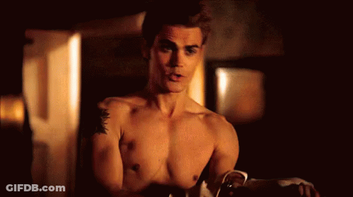 A Shirtless Man With A Tattoo On His Arm Is Standing In A Room . GIF