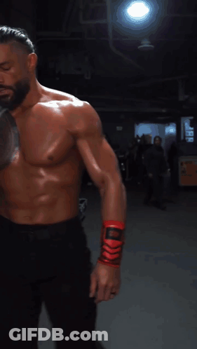 A Shirtless Man With A Tattoo On His Chest Is Wrapping His Wrist With A Red Bandage GIF