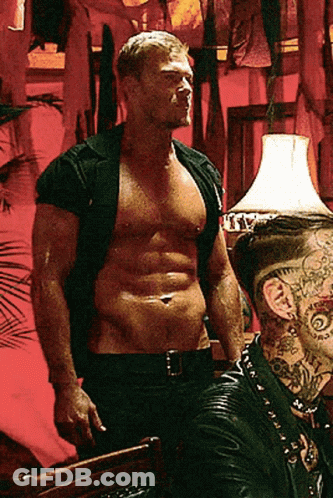 A Shirtless Man With A Tattoo On His Neck Stands Next To Another Man GIF