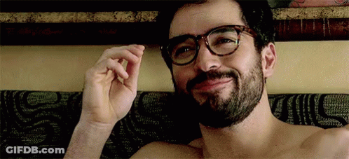 A Shirtless Man With Glasses And A Beard Is Laying On A Bed . GIF