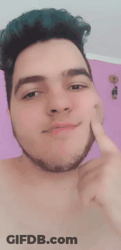 A Shirtless Man With Green Hair And A Beard Touches His Face With His Finger GIF