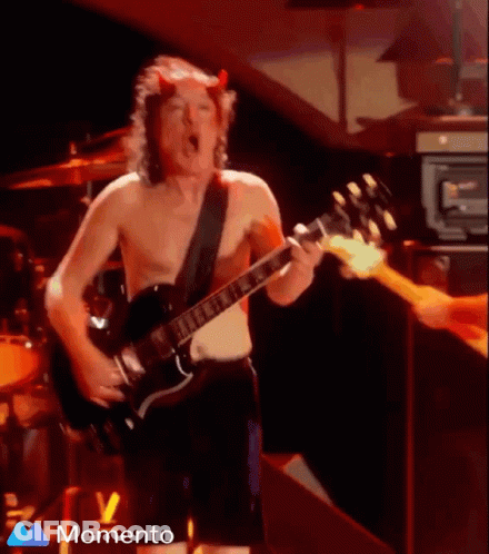 A Shirtless Man With Horns On His Head Is Playing A Guitar On Stage GIF