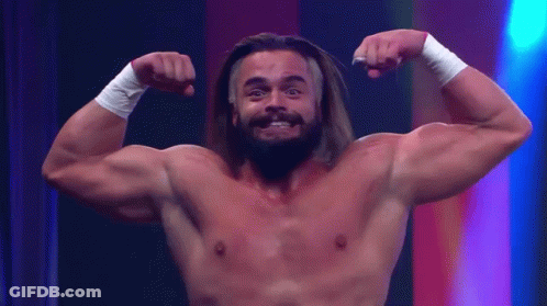 A Shirtless Man With Long Hair And A Beard Flexes His Muscles GIF
