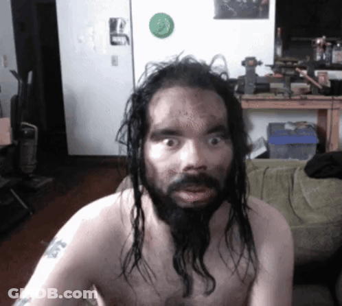 A Shirtless Man With Long Hair And A Beard Has A Tattoo On His Arm That Says ' A ' On It GIF