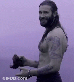 A Shirtless Man With Long Hair And A Beard Is Holding A Bird In His Hand . GIF