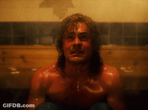 A Shirtless Man With Long Hair Is Sitting In A Bathroom GIF