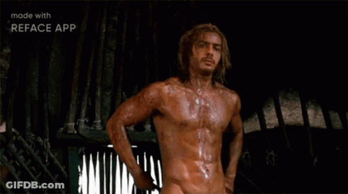 A Shirtless Man With Long Hair Is Standing In Front Of A Fence In A Dark Room . GIF