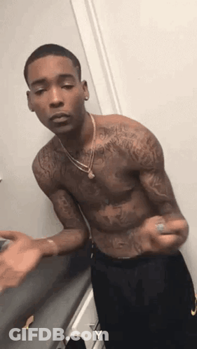 A Shirtless Man With Tattoos On His Arms And Chest Is Standing In A Room . GIF