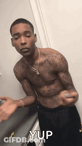 A Shirtless Man With Tattoos On His Arms And Chest Is Standing In A Room . GIF