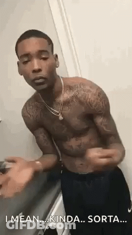 A Shirtless Man With Tattoos On His Arms And Chest Is Standing In Front Of A Door . GIF