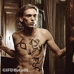 A Shirtless Man With Tattoos On His Chest Is Looking At Himself In A Mirror GIF