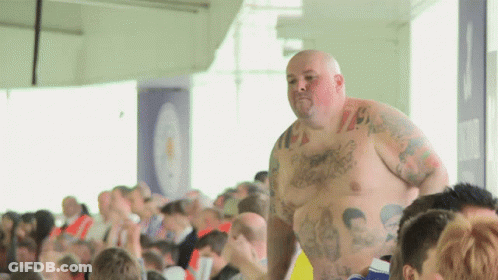 A Shirtless Man With Tattoos On His Chest Stands In Front Of A Crowd Of People GIF