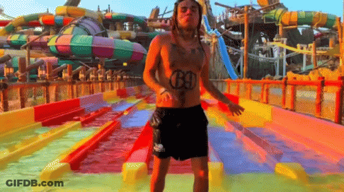 A Shirtless Man With The Number 69 On His Chest Is Standing In Front Of A Water Slide GIF