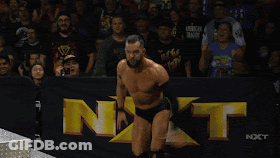 A Shirtless Wrestler In A Wrestling Ring With Nxt Written On The Wall Behind Him GIF