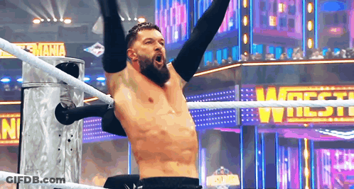 A Shirtless Wrestler Is In A Wrestling Ring With His Arms In The Air . GIF
