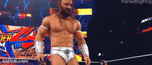 A Shirtless Wrestler Is Standing In A Ring Holding A Microphone . GIF