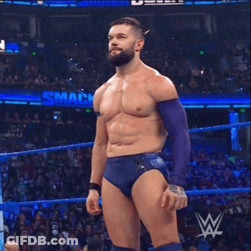 A Shirtless Wrestler Is Standing In A Wrestling Ring With A Smack Down Sign Behind Him GIF