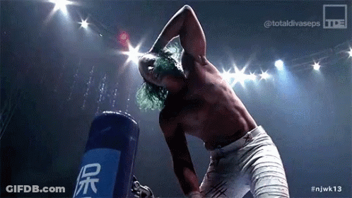 A Shirtless Wrestler Is Standing In Front Of A Blue Bag That Says ' Njwk13 ' On It GIF