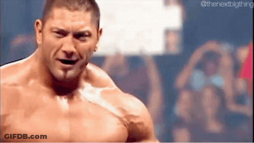 A Shirtless Wrestler Is Standing In Front Of A Crowd And Looking At The Camera . GIF