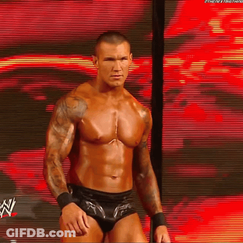 A Shirtless Wrestler Is Standing In Front Of A Large Screen With A W Logo On It GIF