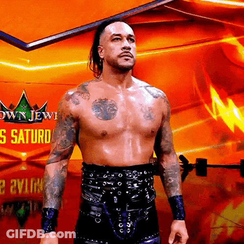 A Shirtless Wrestler Is Standing In Front Of A Sign That Says Crown Jewel Saturday GIF