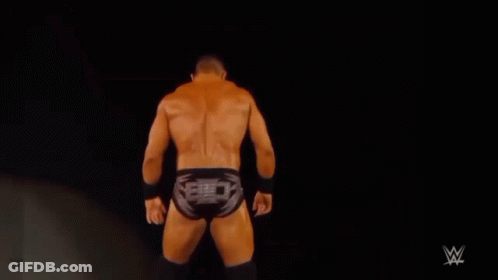 A Shirtless Wrestler Is Standing On A Stage In Front Of A Black Background . GIF