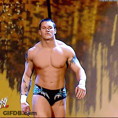 A Shirtless Wrestler Is Walking On A Stage With A W Logo In The Corner GIF