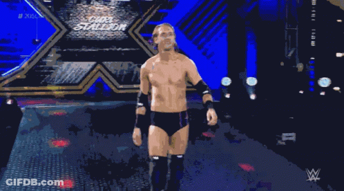 A Shirtless Wrestler Stands In A Dark Room With A Wwe Logo In The Background GIF