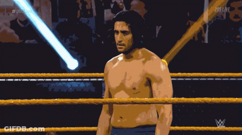 A Shirtless Wrestler Stands In A Wrestling Ring With A Referee Behind Him And 205 Live Written On The Bottom GIF