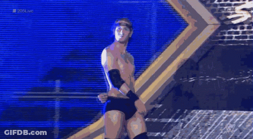 A Shirtless Wrestler Stands In Front Of A Brick Wall With The Hashtag # 20Live On The Bottom GIF