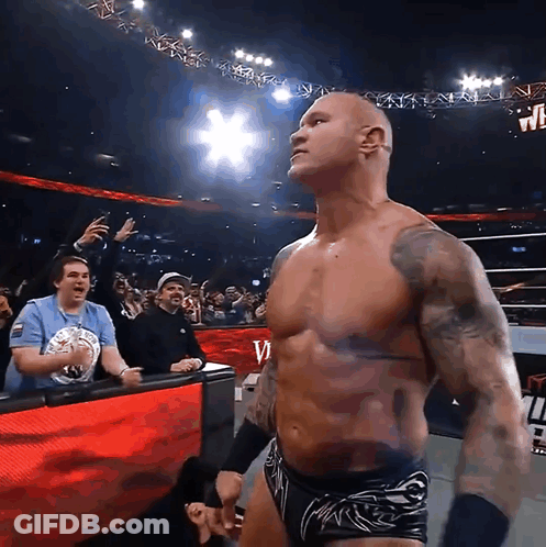 A Shirtless Wrestler Stands In Front Of A Crowd And A Sign That Says W On It GIF