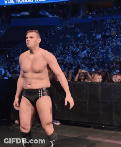 A Shirtless Wrestler Stands In Front Of A Crowd With A Sign That Says Live Holiday Tour GIF