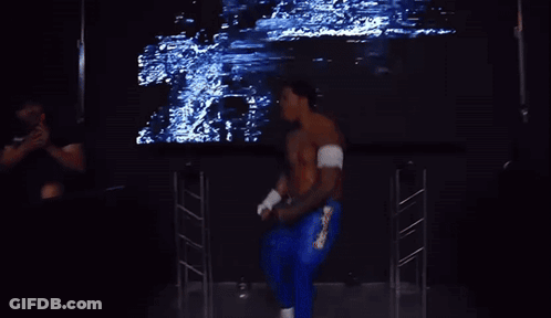 A Shirtless Wrestler Stands In Front Of A Large Screen That Says Zilla GIF