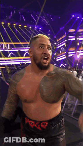 A Shirtless Wrestler Wearing A Belt With The Letter G On It Stands On A Stage GIF