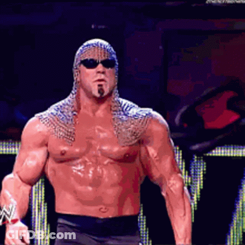 A Shirtless Wrestler Wearing Sunglasses And A Chain Mail Cape GIF