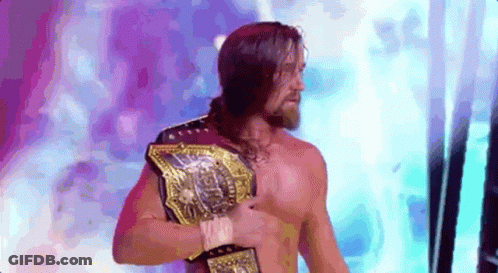 A Shirtless Wrestler With A Beard Is Holding A Championship Belt . GIF