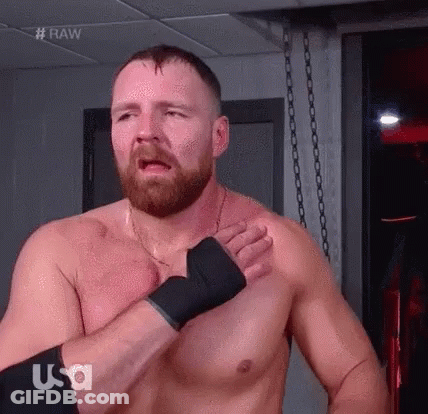 A Shirtless Wrestler With A Beard Is Standing In A Room With His Hands On His Chest . GIF