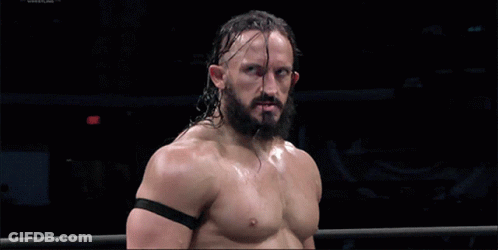 A Shirtless Wrestler With A Beard Stands In A Ring With A Black Band Around His Arm GIF