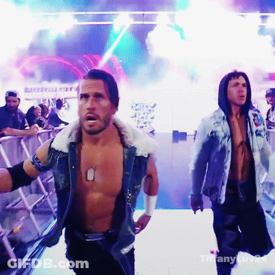 A Shirtless Wrestler With A Dog Tag On His Chest Is Walking Across A Stage GIF
